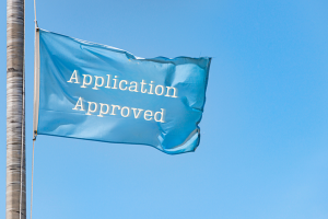 A blue flag with the phrase 'Application Approved,' symbolizing the successful completion of the license and permit bond application process in South Dakota.