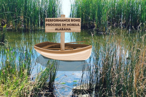 A small wooden boat floating in a marshy area surrounded by tall reeds, with a wooden sign that says 'Performance Bond Process in Mobile, Alabama'.