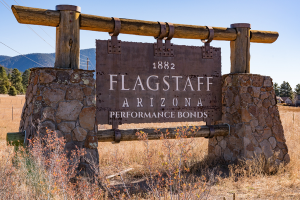 Flagstaff, Arizona 1882 wooden sign promoting performance bonds, set against a rustic stone frame and desert landscape backdrop, representing historical and modern-day bond requirements in Flagstaff.