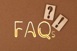 Wooden blocks with question and exclamation marks on a corkboard next to neon-lit 'FAQs,' symbolizing frequently asked questions about performance bonds.