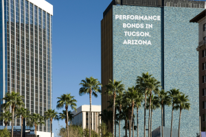 High-rise buildings in Tucson, Arizona with 'Performance Bonds in Tucson, Arizona' text on the facade, surrounded by palm trees and a clear blue sky.