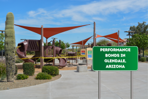 A photo of a modern playground in Glendale, Arizona, with cacti and shade structures, featuring a green sign that reads "Performance Bonds in Glendale, Arizona." This represents construction compliance and public infrastructure in the city.