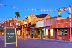 Old Town Scottsdale street at twilight with performance bonds signboard. A scenic view of Old Town Scottsdale, Arizona, featuring historic buildings under string lights, with a sign reading 'Performance Bonds in Scottsdale, Arizona'.