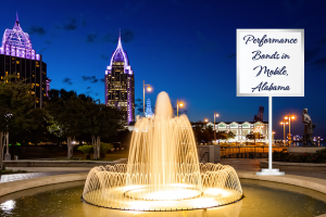 Night view of downtown Mobile, Alabama, with a brightly lit fountain in the foreground and city skyscrapers in the background, featuring a sign that reads 'Performance Bonds in Mobile, Alabama'.