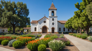 an image of Mission San Jose in Fremont, CA, showcasing the historic adobe church, bell tower, and surrounding gardens. Include visitors in modern attire exploring the site to highlight the fusion of past and present.