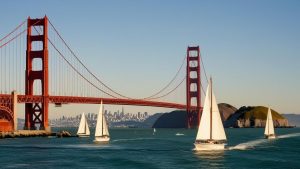 Iconic view of the Golden Gate Bridge in San Francisco, California, with sailboats cruising through the bay under a clear blue sky.