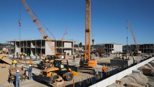 Active construction site in Arcadia, California showing cranes, construction equipment, and workers building large commercial structures.