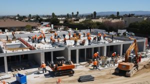 A bustling construction site in Azusa, California, featuring workers in orange safety vests and heavy equipment. The image highlights the city's growing development projects and infrastructure expansion.