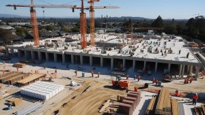 Baldwin Park, California construction workers on a bustling project site with cranes and building materials under a clear blue sky.