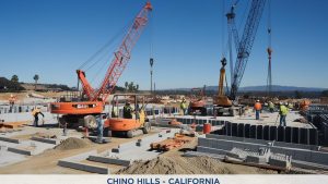 Construction site in Chino Hills, California, showcasing active cranes, heavy machinery, and workers building infrastructure under a clear blue sky.