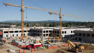 Active construction site in Fort Collins, Colorado, with cranes, machinery, and workers building a commercial structure under a clear blue sky.