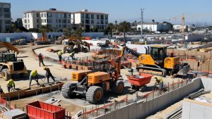 Active construction site in Gardena, California, showcasing heavy machinery and workers building infrastructure with a backdrop of modern buildings.