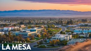 Panoramic view of La Mesa, California, at sunset, showcasing vibrant community structures, tree-lined streets, and distant mountains.