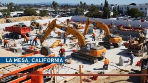 Construction site in La Mesa, California, featuring workers, heavy machinery, and equipment during an active building project.