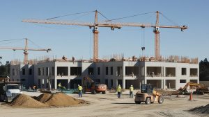 Construction site in Lake Forest, California, showcasing a multi-story building under development with cranes and construction workers, highlighting the region's growth and infrastructure expansion.