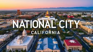 Aerial view of downtown National City, California, with prominent civic buildings, tree-lined streets, and a vibrant cityscape during sunset.