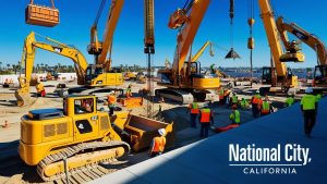 Construction site in National City, California, featuring cranes, heavy machinery, and workers in safety gear completing a large-scale commercial project.