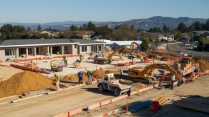 Active construction zone in San Luis Obispo, California, featuring workers, heavy equipment, and new building foundations under construction.