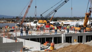 A busy construction site in San Gabriel, California, showcasing workers in safety gear and cranes lifting heavy materials. Represents development and infrastructure projects requiring performance bonds.