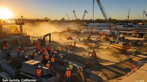 Extensive construction site in San Jacinto, California, with workers and heavy equipment operating under a vibrant sunset sky, highlighting the city's development projects.