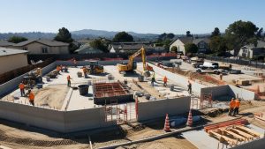 Construction site in Santee, California, showcasing workers and heavy equipment actively building foundations in a residential area with scenic hills in the background.