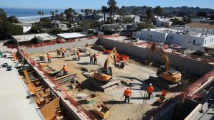 Aerial view of a construction site near the coastline in Tulare, California, showcasing excavators and workers actively building residential structures.