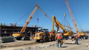 Heavy equipment including cranes and bulldozers at a commercial construction project in Citrus Heights, California, with workers in safety vests coordinating operations.