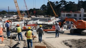 Construction workers in bright safety vests and helmets at a modern building site in Cypress, California, emphasizing structured project management and the role of performance bonds.