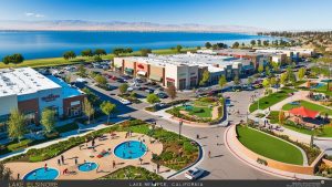 A vibrant shopping area near Lake Elsinore, California, featuring a view of the lake, landscaped park, and retail stores, representing the development and community amenities around Menifee.