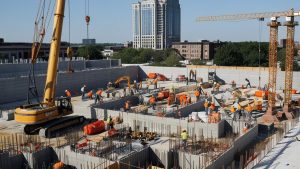 Construction workers collaborating on-site in Aurora, Illinois, with cranes and scaffolding surrounding a large commercial building under development.