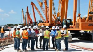 Group of construction workers and managers wearing hard hats and safety vests reviewing blueprints at a construction site in Jupiter, Florida.