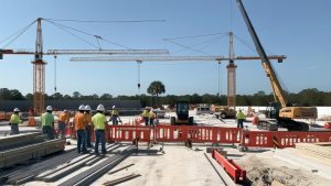 Construction site in Kissimmee, Florida, featuring workers in safety vests and cranes actively building infrastructure under a clear blue sky.