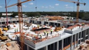 Active construction site in Lauderhill, FL, featuring cranes and workers completing a commercial building project under clear blue skies.