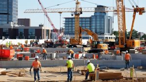 Workers actively building a structure on a bustling construction site in Naperville, Illinois, with cranes and modern buildings in the background.