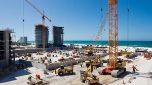 Construction workers building a vibrant beachfront property in North Miami Beach, Florida, with the turquoise ocean in the background.