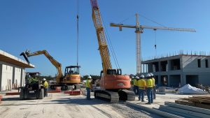 Construction site in Titusville, Florida with cranes, excavators, and workers in safety gear managing an active building project under a clear blue sky.