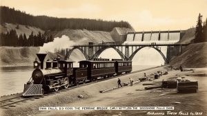 Historical photograph of a train crossing the Perrine Bridge near the Shoshone Falls Dam in Twin Falls, Idaho, showcasing early 20th-century engineering and natural beauty.