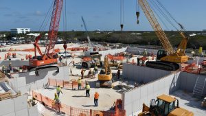 Busy construction site in Boynton Beach, Florida, featuring cranes, construction vehicles, and workers actively building infrastructure under a clear blue sky.