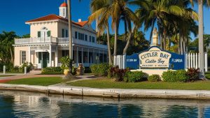 Welcome to Cutler Bay, Florida sign surrounded by palm trees and greenery, with a historic Southern-style building in the background, reflecting the area’s charm and architecture.