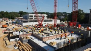 Construction site in Danbury, Connecticut, showcasing cranes, workers in safety gear, and ongoing building projects under sunny skies.