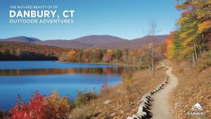 Scenic view of a trail along a vibrant autumn lake in Danbury, Connecticut, with colorful foliage and distant rolling hills.