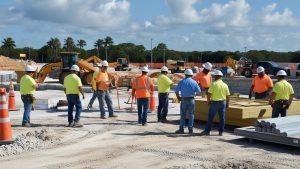 Group of construction workers in safety gear coordinating on-site at a development project in North Port, Florida, with heavy machinery and materials in the background.