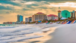 Scenic beachfront in Panama City, Florida, with colorful umbrellas, gentle waves, and modern high-rise buildings during sunset.