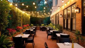 Cozy outdoor dining area in Savannah, Georgia, featuring string lights, vibrant flower arrangements, and neatly arranged tables on a brick patio.