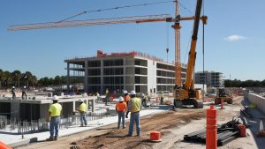 Active construction site in St. Petersburg, Florida, showcasing workers in safety gear, cranes, and a partially completed building structure under sunny skies.