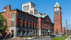 A historic red-brick building and clock tower in downtown Waterbury, Connecticut, showcasing the city's architectural charm on a sunny day.