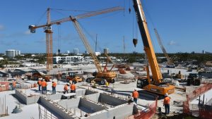 Active construction site in West Palm Beach, Florida, showcasing cranes, heavy machinery, and workers in orange safety gear building a large-scale development project.