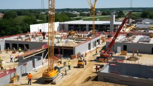 A bustling construction site in Jeffersonville, Indiana, with cranes, workers, and heavy machinery actively building a commercial complex amidst green surroundings.