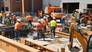 Construction workers wearing safety gear working on a construction site in Hanover Park, Illinois, with heavy equipment and building materials in the background.