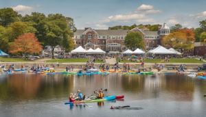 Scenic view of the Mystic River in Medford, Massachusetts, featuring kayakers and a lively outdoor festival with tents, local vendors, and community engagement.